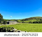 A charming stone cottages nestled in the rolling green hills of the countryside. The bright blue sky and scattered clouds add to the idyllic rural setting, evoking a sense of simplicity and peace.