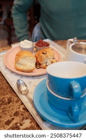 A charming table set for high tea in a cozy cafe, featuring two cups of tea and a selection of freshly baked scones with clotted cream and jam.