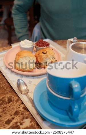 A charming table set for high tea in a cozy cafe, featuring two cups of tea and a selection of freshly baked scones with clotted cream and jam.
