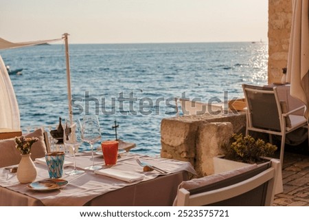 A charming table set for two invites diners to enjoy a sunset meal overlooking the shimmering waters of the Adriatic Sea in Rovinj, Croatia. The atmosphere is warm and serene.