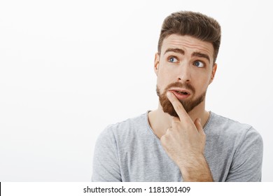 Charming Thoughtful, Charismatic Man Trying Think Up Solution. Creative Handsome Brunet Boyfriend With Beard And Blue Eyes Raising Eyebrows Looking At Upper Left Corner Touching Lip, Thinking