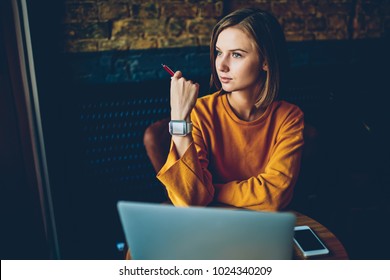 Charming thoughtful hipster girl with modern smartwatch on hand looking out of window and thinking on creative ideas for developing own training project sitting at computer in coffee shop - Powered by Shutterstock