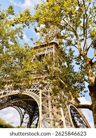  Charming view of the Eiffel Tower partially hidden behind lush green trees, creating a natural frame for the iconic Paris landmark.
