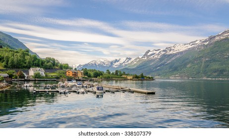 Charming view to small port with several boats in Norwegian village on the bank of fjord with blue sky with feather clouds and mountain peaks with snow caps in the background, Hardangerfjorden, Norway - Powered by Shutterstock