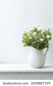 A charming white ceramic pitcher overflows with small white blossoms and green foliage, set against a soft, light background.