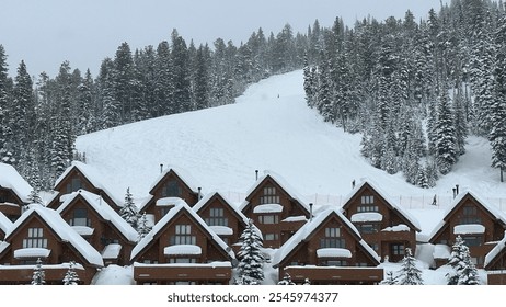 A charming winter town nestled at the base of a snowy mountain slope, with cozy wooden cabins blanketed in snow. The surrounding pine trees and ski hill create a picturesque winter wonderland scene. - Powered by Shutterstock