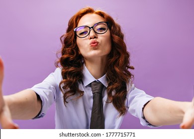 Charming Woman In Blue Shirt And Eyeglasses Blows And Takes Selfie. Lovely Girl With Wavy Ginger Hair In Glasses And Black Tie Looking Into Camera