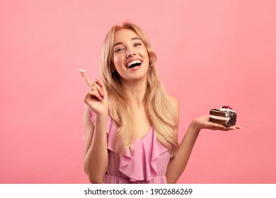 Charming Woman In Dress Tasting Delicious Birthday Cake On Pink Studio Background. Attractive Blonde Lady Celebrating Holiday, Enjoying Yummy Dessert. Festive Concept