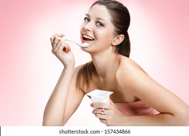 Charming Woman Eating Yogurt / Studio Photography Of Brown-eyed Brunette Girl Holding Spoon And A Container Of Yogurt - On Blurred Background 