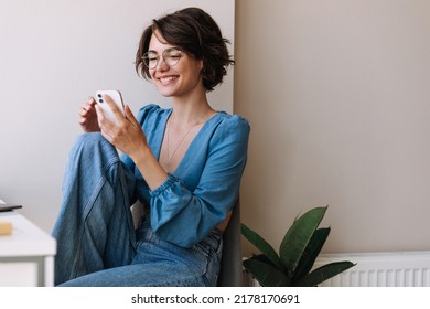 Charming woman holding phone at home . Caucasian smiling brunette woman looking and chatting on smartphone sitting on the floor. Concept of lifestyle, use technology  - Shutterstock ID 2178170691