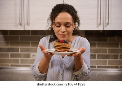 Charming woman holding a plate of delicious homemade freshly baked pancakes garnished with wild berries. Beautiful young dark-haired curly housewife with cooked pancakes for Shrovetide. Shrove Tuesday - Shutterstock ID 2108741828