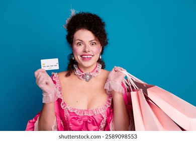 Charming woman in pink baroque dress holds shopping bags and card against blue background