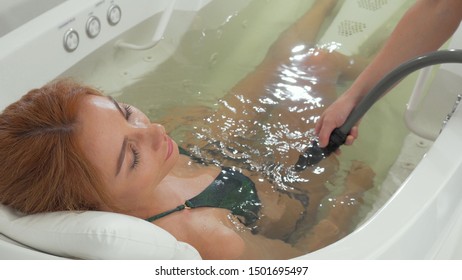 Charming woman relaxing while getting hydromassage at spa. Sliding shot of a gorgeous woman enjoying whirl pool bath. Spa therapist doing hydro massage on female client