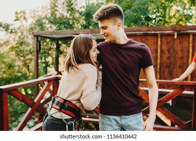 Charming Woman In Safety Harness With Young Boyfriend Preparing For Zip Line Ride And Looking Scared While Having Fun In Park