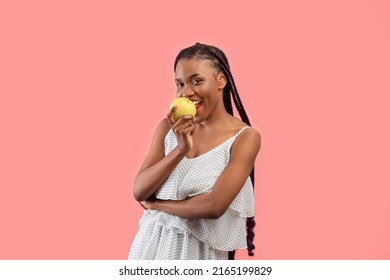 Charming Young African American Woman Eating Ripe Green Apple On Pink Studio Background. Lovely Millennial Black Female Enjoying Delicious Fruit. Vitamins For Healthy Teeth And Beautiful Skin