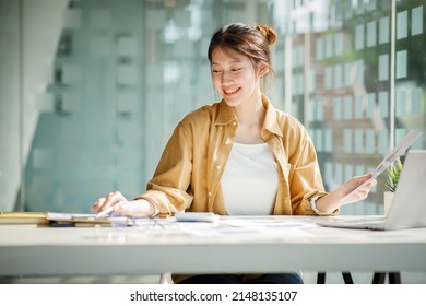 Charming Young Asian Businesswoman Sitting On Laptop Computer In The Office, Making Report Calculating Balance Internal Revenue Service Checking Document.