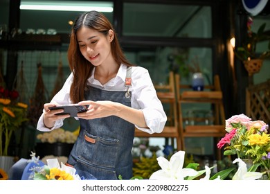 Charming Young Asian Female Florist Or Flower Shop Worker Photographing Flower Arrangement With Her Mobile Phone.