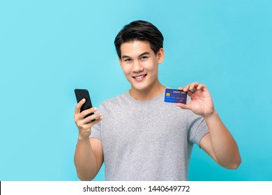 Charming Young Asian Man Having Fun Paying His Online Shopping Through Credit Card Isolated On Light Blue Background