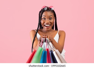 Charming Young Black Woman With Afro Bunches Holding Lots Of Shopping Bags On Pink Studio Background. Portrait Of Cheerful Millennial Lady Demonstrating Her Purchases, Buying Goods On Sale