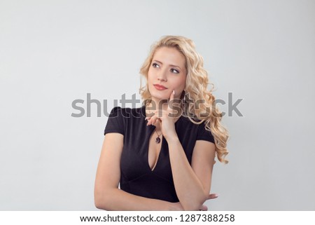 Charming young blond woman in black dress dreaming and looking away daydreaming. Caucasian Business person in black formal dress, long blond curly hair isolated on light grey gray studio background