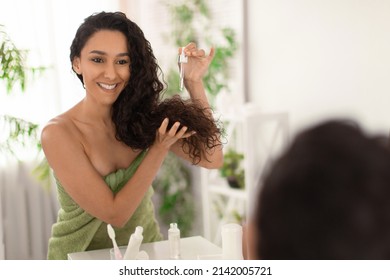 Charming Young Brunette Woman Applying Serum On Damaged Dry Hair Near Mirror At Home, Blank Space. Organic Cosmetics For Haircare, Natural Treatment Procedure, Beauty Routine Concept