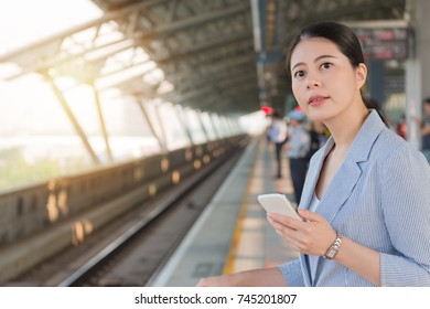 Charming Young Business Woman Holding Smart Phone Standing On The Platform And Waiting For The Taiwan High Speed Rail On A Sunny Day.