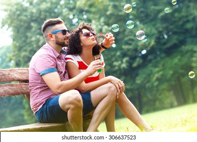 Charming young couple sitting on bench in the park and blowing bubbles. - Powered by Shutterstock