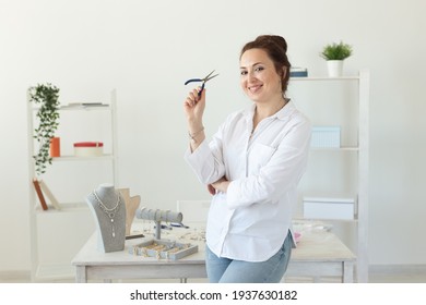 Charming young enthusiastic caucasian woman making beautiful unique costume jewelry while sitting at her desk. Concept of hobby and pleasant work