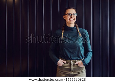 Charming young girl standing indoors with hands in pockets and looking away.