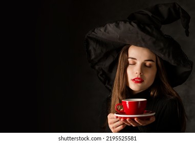 Charming young girl in a witch's hat with a cup of hot coffee in her hands