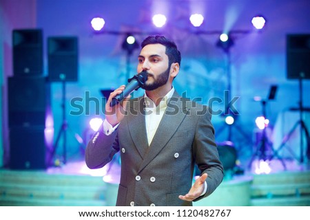Charming young man leading acts at the evening concert in a gray suit under the light of the spotlights
