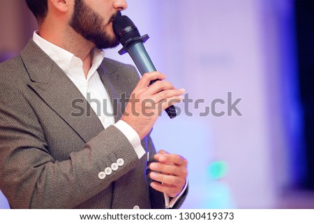Charming young man leading acts at the evening concert in a gray suit under the light of the spotlights.