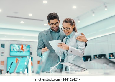 Charming Young Multicultural Couple In Formal Wear Trying Out New Tablet In Tech Store.