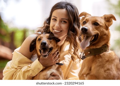Charming young smiling girl is resting in the park with two golden dogs on a sunny day. The girl hugs her pets. Love and affection between owner and pet. Adopting a pet from a shelter. Close-up.