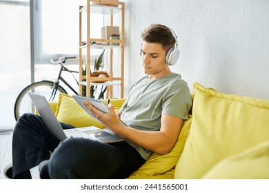 charming young student with headphones and laptop in yellow couch studying and writing in note