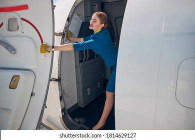 Charming Young Woman Flight Attendant Closing Aircraft Door And Smiling