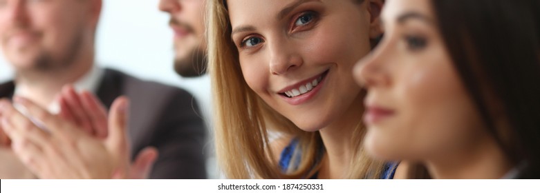 Charming young woman looking at camera and smiling while clapping hands during meeting with colleagues in conference room