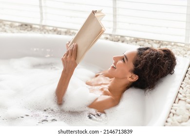 Charming young woman lying in bubble bath, reading book in relaxing atmosphere at home, free space. Beautiful millennial lady enjoying interesting story in bathtub at hotel room - Powered by Shutterstock