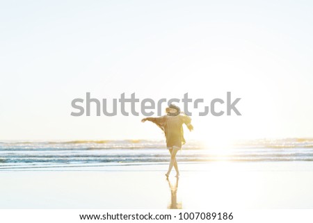 Charming young woman with poncho, hat, sunglasses with cute smile dancing on the beach at sunset in warm weather.
