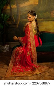 Charming Young Woman Is Sitting On The Sofa. Traditional Indian Wedding Sari And Jewelry.