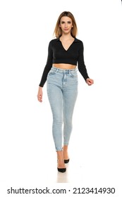 Charming Young Woman Walking In Studio In Black Short Blouse And Blue Jeans On A White Background