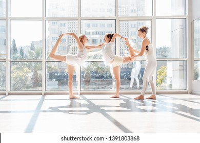 Charming young woman yoga instructor teaches her two students to do natarajasana while standing on one leg of a gymnasium with large windows. Healthy lifestyle concept and regular workouts - Powered by Shutterstock