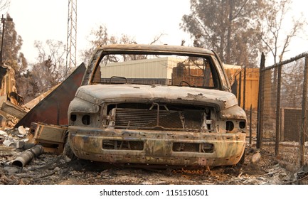 Charred Car Next To Chain Link Fence In Front Of Home Burned To The Ground In The Recent Wild Fire Fire Storm In Redding, CA. Smoke And Ash In The Air As The Fire Continues To Burn Several Miles Away.