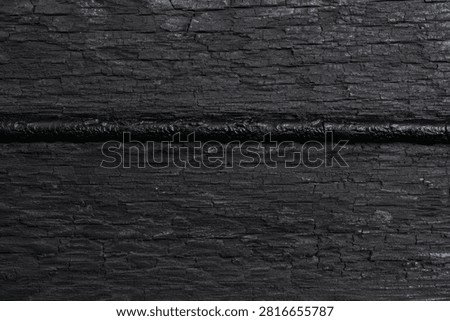 Charred Timber Background. Dark burnt wooden surface showcasing cracked obsidian patterns from fire, symbolizing preservation, resilience, and rustic elegance.