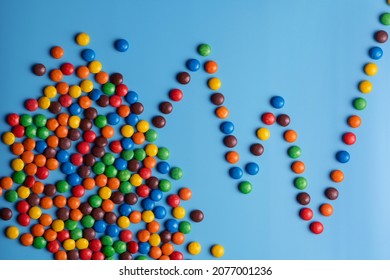 Chart, Graph Made Of Colorful Smarties, Candies On Blue Background. Isolated Color Studio Photo. Illustration Of Tendency To Eat Too Much Sugar Or Calories Intake.