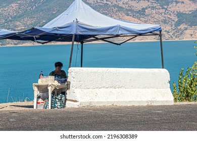 Charvak, Uzbekistan, 08.13.2022. Saleswoman Of Kurt (dried Cheese) Under An Awning By The Road On The Shore Of The Charvak Reservoir In Uzbekistan