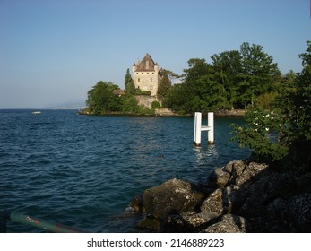Chateau d'Yvoire in medieval village in Haute Savoie, France.

Clear blue sky and lake Geneva (Lac Léman) with green plants and trees surrounding the building and the lake shores.