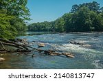 Chattahoochee river at the Jones bridge park in Georgia with some geese in the middle and a few people fishing in the background near the rusted exempt railroad bridge on a sunny day in springtime