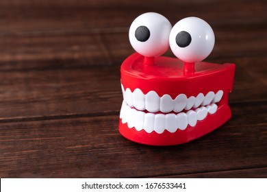 Chattering Teeth Toy With Big Eyes On A Wooden Background With Copy Space. Plastic Red Mouth With White Fangs Is A Concept Of Oral Hygiene And Healthy Teeth