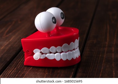 Chattering Teeth Toy With Big Eyes On A Wooden Background With Copy Space. Plastic Red Mouth With White Fangs Is A Concept Of Healthy Teeth And Oral Hygiene